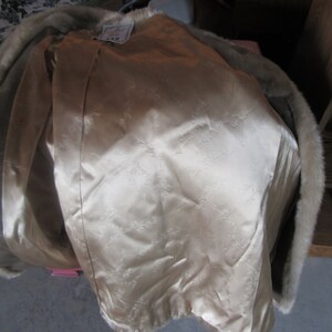 May include: A beige fur coat with a satin lining. The lining has a floral pattern. The coat has a fur collar.