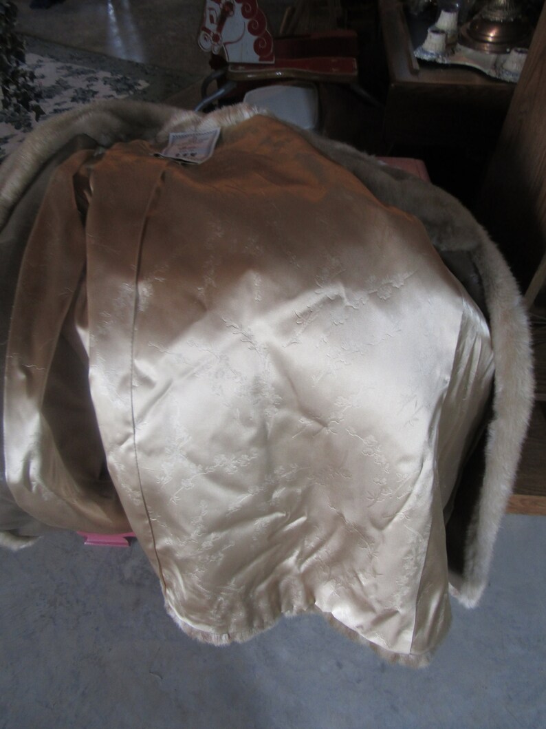May include: A beige fur coat with a satin lining. The lining has a floral pattern. The coat has a fur collar.