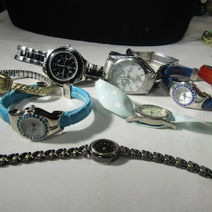 Può includere: Una collezione di otto orologi da polso con vari stili e colori. Gli orologi hanno cinturini di diversi colori, tra cui nero, argento, blu e rosso. Alcuni orologi hanno un quadrante argentato, mentre altri hanno un quadrante nero. Gli orologi sono disposti su una superficie bianca.
