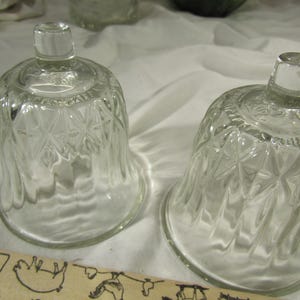 Könnte beinhalten: Zwei durchsichtige Glasglocken mit einem Diamantenmuster. Die Glocken sind leer und stehen auf einer weißen Oberfläche.