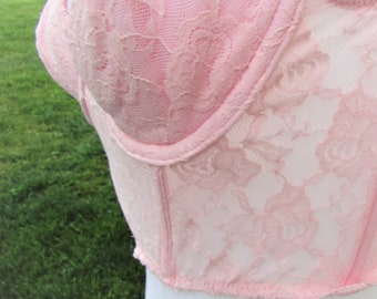 May include: Pink lace bra with a delicate floral pattern. The bra has a boned bodice and adjustable straps.