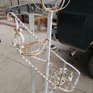 May include: A white metal plant stand with a spiral design and a decorative top. The stand is rusty in places and has a white background.