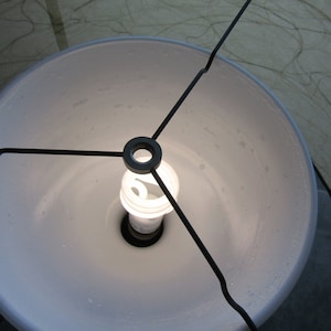 May include: A white lampshade with a black metal frame and a light bulb inside.