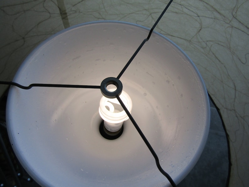 May include: A white lampshade with a black metal frame and a light bulb inside.