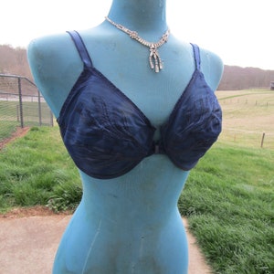 May include: A blue lace bra with a hook and eye closure. The bra is on a mannequin with a rhinestone necklace.