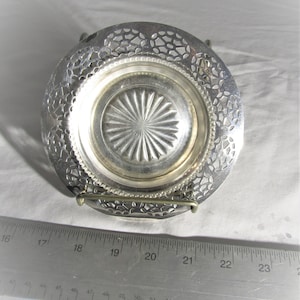 May include: A silver-plated, decorative, openwork dish with a scalloped edge and a raised, starburst-patterned centre. The dish is on a stand.