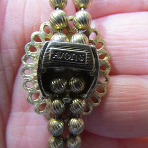 Peut inclure: Collier en ton or avec un fermoir d&eacute;coratif portant l'inscription "AVON" et un motif perl&eacute;.