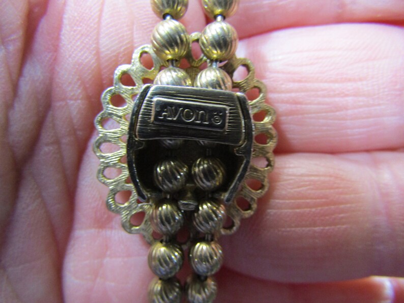 Peut inclure: Collier en ton or avec un fermoir d&eacute;coratif portant l'inscription "AVON" et un motif perl&eacute;.