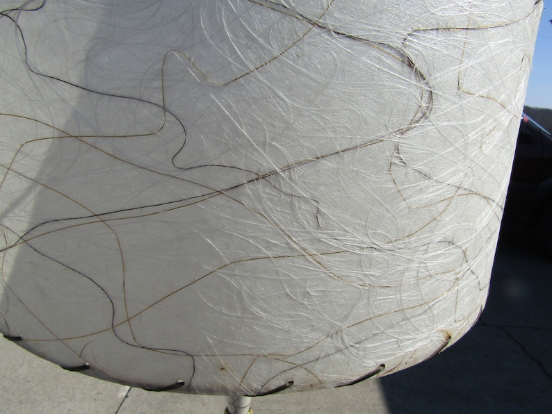 May include: White lampshade with a textured surface and brown lines. The lampshade is made of a material that resembles paper.