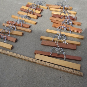 May include: A collection of wooden clothes hangers with metal hooks. The hangers are made of light and dark brown wood. A wooden ruler is also present, showing measurements in inches.