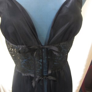 Pu&ograve; includere: Lingerie nera con scollatura profonda e pannello in pizzo in vita. L'indumento presenta una chiusura con fiocco e spalline delicate. Il tessuto sembra essere un materiale morbido e fluido.