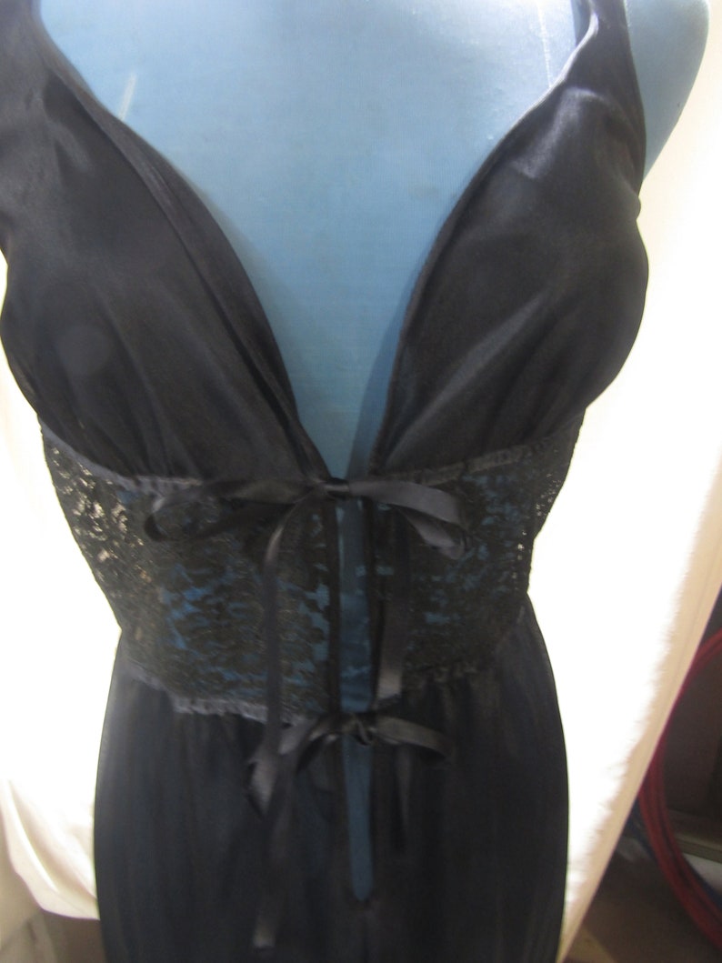 Pu&ograve; includere: Lingerie nera con scollatura profonda e pannello in pizzo in vita. L'indumento presenta una chiusura con fiocco e spalline delicate. Il tessuto sembra essere un materiale morbido e fluido.