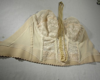 Puede incluir: Un sujetador beige sin tirantes con detalles de encaje y un collar de perlas.