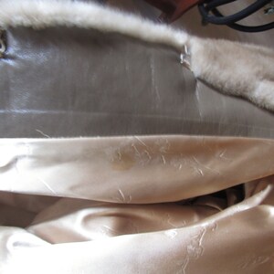 May include: The inside of a fur coat with a brown leather lining and a white satin lining.