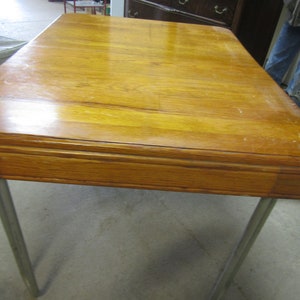 Puede incluir: Una mesa rectangular de madera con acabado marrón claro y esquinas redondeadas. La mesa tiene cuatro patas de metal plateado. La mesa mide aproximadamente 91 cm de largo y 61 cm de ancho.