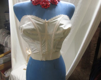 May include: A white strapless corset with a zipper closure and lace trim. The corset is on a blue mannequin.