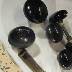 Könnte beinhalten: Sechs schwarze Keramik-Türknöpfe mit glänzender Oberfläche. Einige der Knöpfe sind an Metallstangen befestigt.