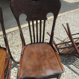 Puede incluir: Silla de madera marrón oscuro con respaldo y asiento curvos. La silla tiene un recorte decorativo en la parte superior del respaldo y listones verticales. El asiento es de un tono marrón más claro. La silla forma parte de un conjunto.