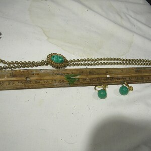 Peut inclure: Un collier en or avec un pendentif en pierre verte et des boucles d'oreilles assorties en pierre verte. Le collier est compos&eacute; de petites perles dor&eacute;es et le pendentif est une pierre verte ronde sertie dans un cadre en or. Les boucles d'oreilles sont &eacute;galement des pierres vertes rondes serties dans des cadres en or.
