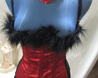 May include: A red satin corset with black lace trim and a black feather trim. A red flower necklace with rhinestone accents adorns the mannequin. The corset is displayed on a blue mannequin.
