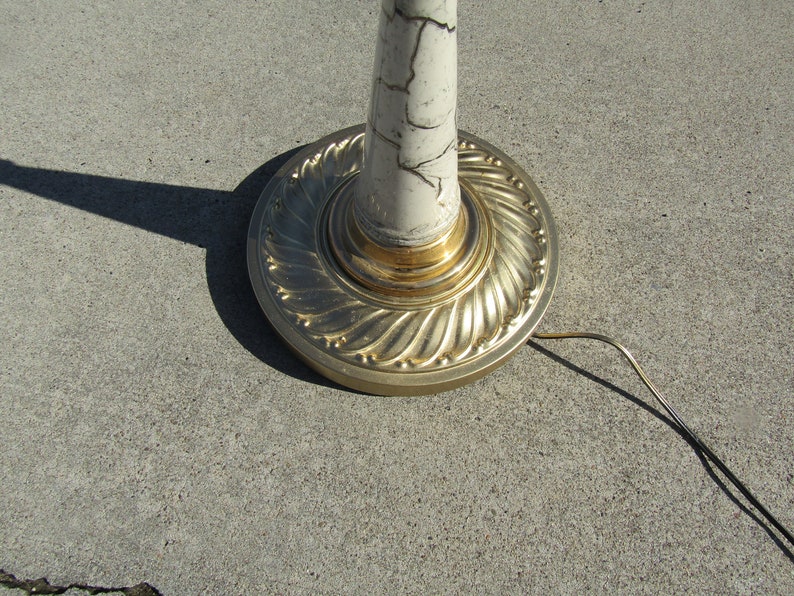 May include: A white floor lamp with a gold base and a marbled design. The lamp has a cord and plug.