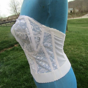 May include: White lace corset with a blue background. The corset has a scalloped edge and is made of a delicate fabric.