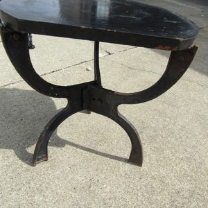 Könnte beinhalten: Ein kleiner, antiker schwarzer Tisch mit einer dunklen, ovalen Tischplatte. Der Tisch hat ein einzigartiges, gebogenes Metallgestell. Die Tischplatte ist etwa 61 cm lang und 46 cm breit.
