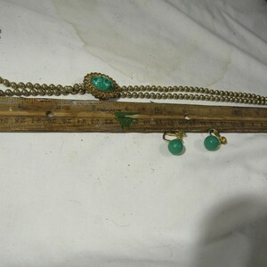 Peut inclure: Un collier en or avec un pendentif en pierre verte et des boucles d'oreilles assorties en pierre verte. Le collier mesure 76 cm de long et a un pompon &agrave; une extr&eacute;mit&eacute;.