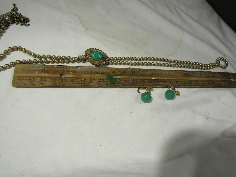 Peut inclure: Un collier en or avec un pendentif en pierre verte et des boucles d'oreilles assorties en pierre verte. Le collier mesure 76 cm de long et a un pompon &agrave; une extr&eacute;mit&eacute;.