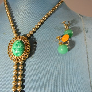 Peut inclure: Un collier en or avec un pendentif en pierre verte et blanche et des boucles d'oreilles assorties en pierre verte et blanche. Le collier est compos&eacute; de perles dor&eacute;es et le pendentif est une pierre ronde sertie dans un cadre en or. Les boucles d'oreilles sont &eacute;galement des pierres rondes serties dans des cadres en or.