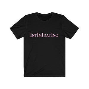 Puede incluir: Camiseta negra de manga corta con la palabra "INTIMIDATING" impresa en rosa en la parte delantera.