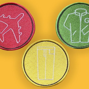 May include: Three embroidered patches with white outlines on a yellow background. The patches are circular, with a red airplane, a green jacket, and yellow pants. Each patch has a black border.
