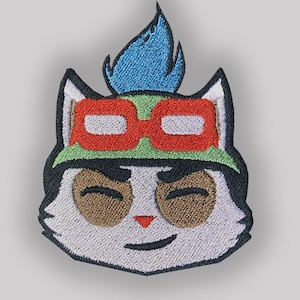 以下が含まれることがあります： 白い猫の刺繍パッチ。黒い目と茶色の鼻をしています。猫は緑色の帽子をかぶり、赤いゴーグルと青い炎を頭に乗せています。