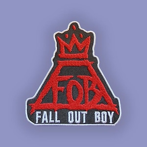 Może przedstawiać: Haftowana naszywka z nazwą zespołu "Fall Out Boy" i "FOB" w kolorze czerwonym, z motywem korony. Naszywka ma czarne tło i białą obwódkę, na tle lawendowego koloru.