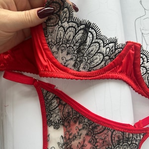 Op de afbeelding: Rode lingerie set met een beha en bijpassende slip. De beha en slip zijn afgewerkt in rood en hebben zwarte bloemen kanten details. De beha heeft verstelbare bandjes. De set wordt gepresenteerd op een witte ondergrond.