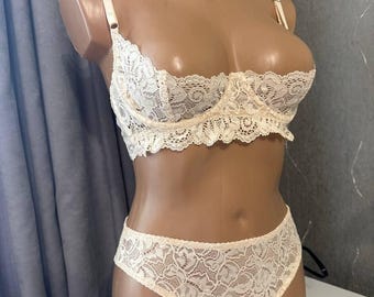 May include: Ivory lace lingerie set, comprising a bra and matching briefs. The bra features adjustable straps and a delicate lace design. The briefs have a high-waisted cut with a matching lace pattern. The set is displayed on a mannequin.