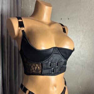 May include: Black satin and lace lingerie top with adjustable straps and a hook and eye closure. The top has a sweetheart neckline and a bustier style.