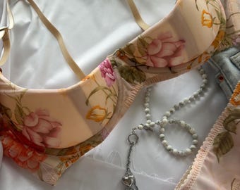 May include: A floral print bra with a delicate lace trim. The bra is made of a soft, sheer fabric and features a delicate floral pattern in shades of pink, yellow, and orange. The bra is paired with a matching panty.