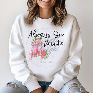 Puede incluir: Sudadera blanca con un gr&aacute;fico de zapatillas de ballet rosas y el texto "Always On Pointe" en letras negras.