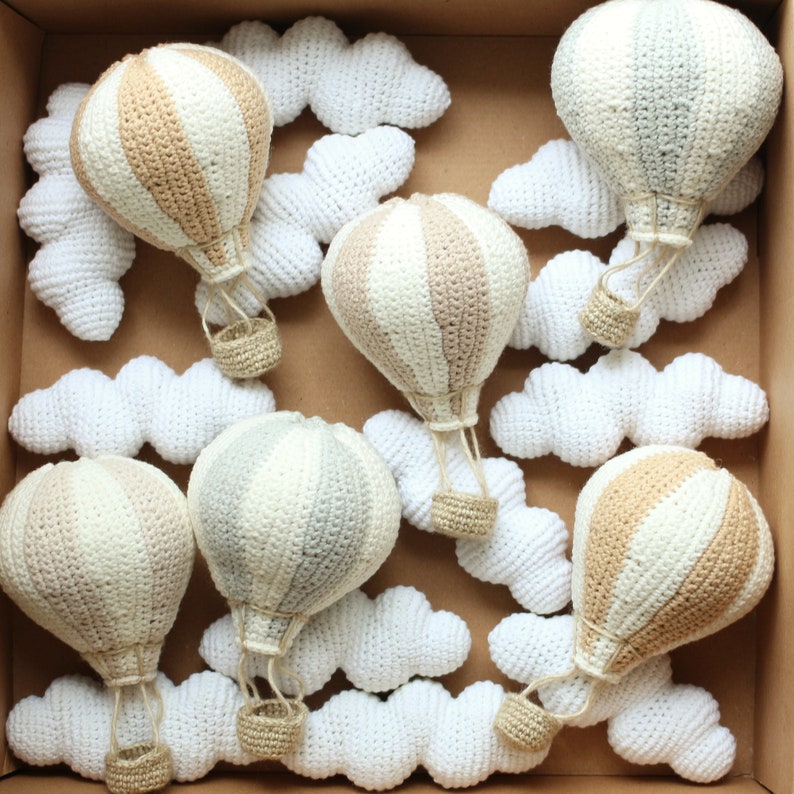 May include: A set of crocheted hot air balloons in beige and gray with white crocheted clouds. The balloons have a striped pattern and are hanging from the ceiling.