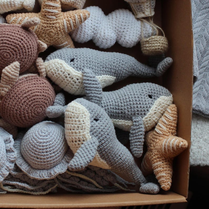 May include: A collection of crocheted stuffed toys, including whales, starfish, and a cloud. The toys are made in shades of grey, brown, and beige.