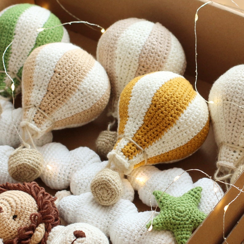 May include: A set of crocheted hot air balloons and clouds in various colors, including white, beige, yellow, and green. The balloons are decorated with stripes and have a textured, knitted appearance.