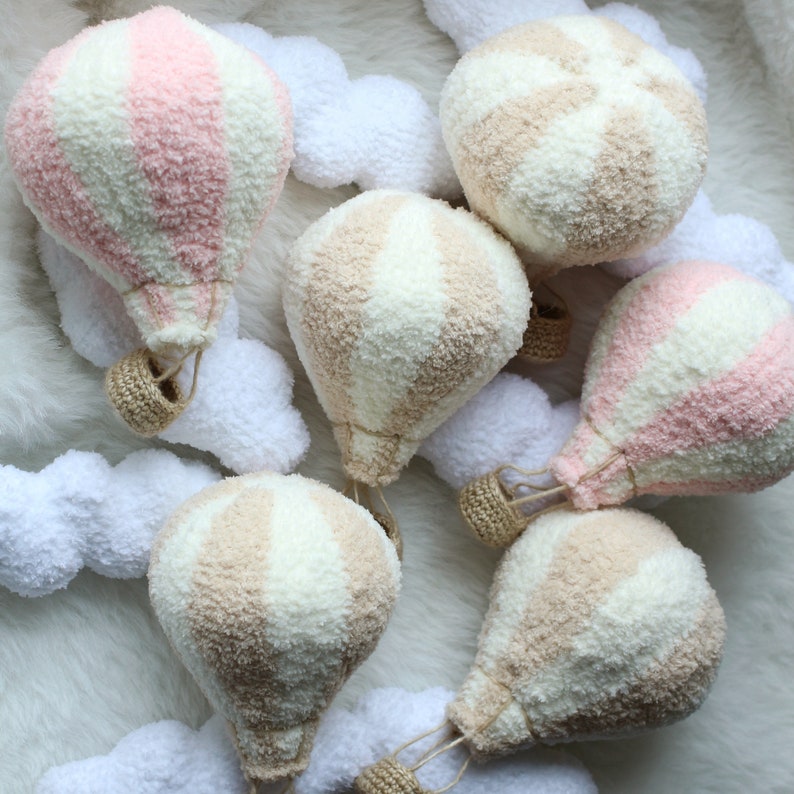 May include: A set of six plush hot air balloons in pink and beige with white stripes. The balloons are made of a soft, fuzzy fabric and have a crocheted basket.