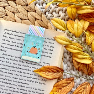May include: A bookmark with a fall-themed design featuring a pumpkin and leaves. The bookmark has the text "Fall into Jesus" and "He Never Leaves".