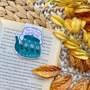 May include: A teal blue teapot with pink and white flowers and hearts on it. The teapot is on a bookmark with the text "Tea is always a good idea".