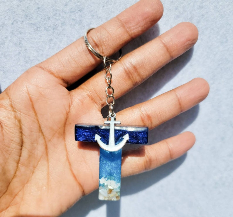 May include: A resin keychain in the shape of the letter "T" with a nautical theme. The top section is dark blue, the middle is light blue with white accents, and the bottom has small white and tan pieces. A silver anchor charm is attached.