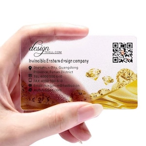 May include: A clear plastic business card with a gold background and a design of diamonds. The text on the card reads "design TMALL.COM Invinciblo Eastern design company Shenzhen City, Guangdong Province, Futian District TEL:4000 000 640 FAX:4000 900 6.0 Email mixgpin@taobao.cn ewob.tcobro.com"
