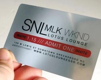 May include: A silver metal card with black text that reads "SNL MLK WKND LOTUS LOUNGE INVITE 1.15 /// ADMIT ONE INVITE 120 W LEWIS ST DOWNTOWN GREENSBORO NC WWW.LOTUSLOUNGEGSO.COM".