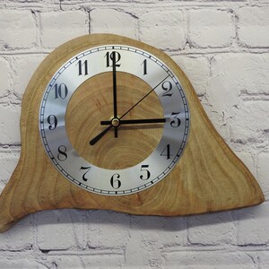 May include: A wooden wall clock with a unique, irregular shape. The clock face is silver with black Roman numeral markings and black hands.