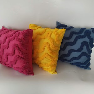 May include: Three decorative throw pillows with a wavy pattern. The pillows are pink, yellow, and blue.
